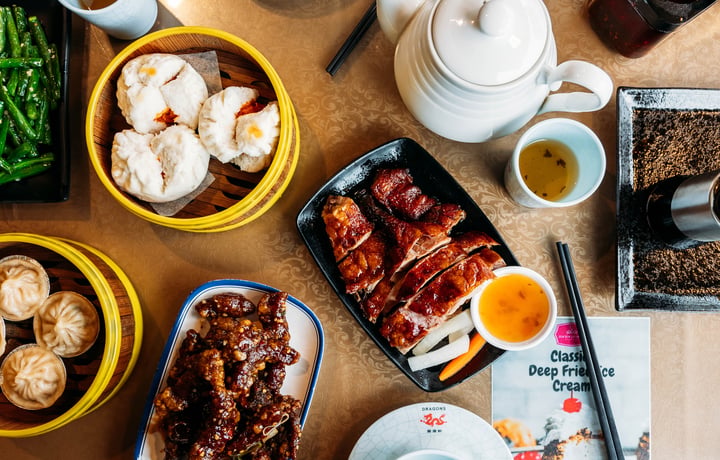 Table full of plates of Asian dishes and chopsticks.