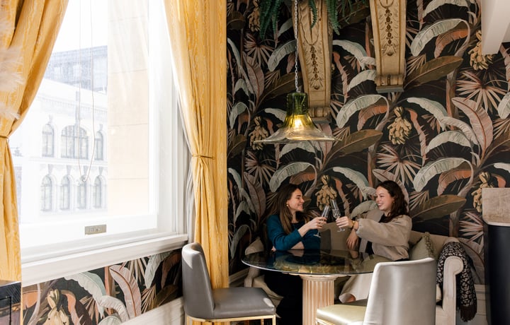 Two women toasting their wine glasses sitting at a table.