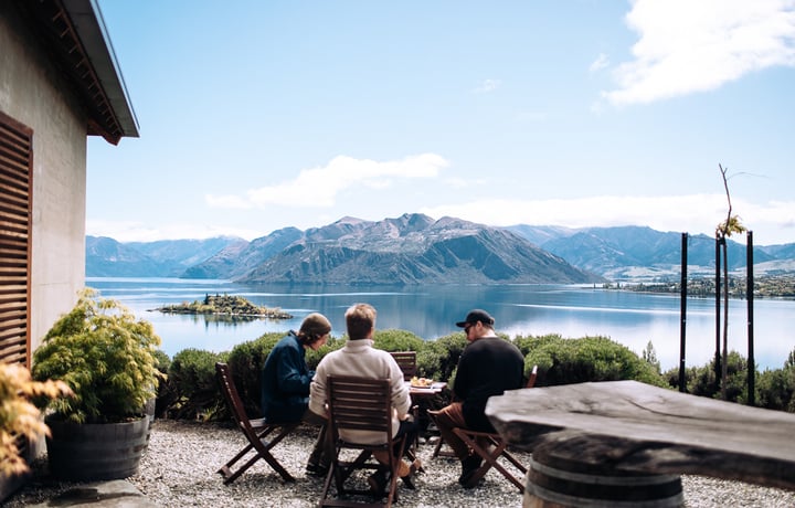 Three men are sitting at an outdoor table overlooking the lake.