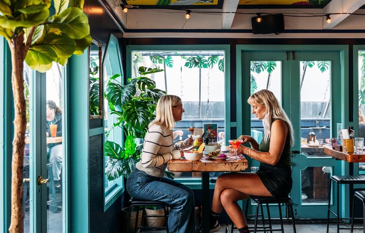 Two women dining at a high table inside a green painted room.