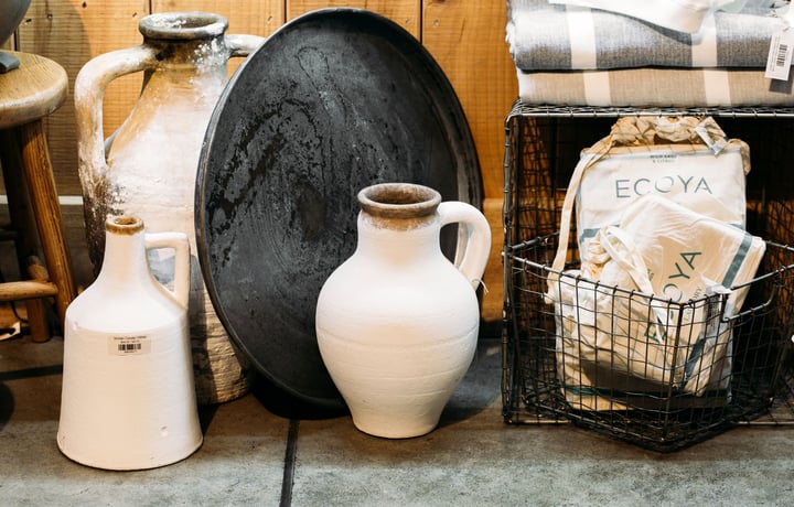 Two tall white concrete look vases on the floor next to a wire basket.