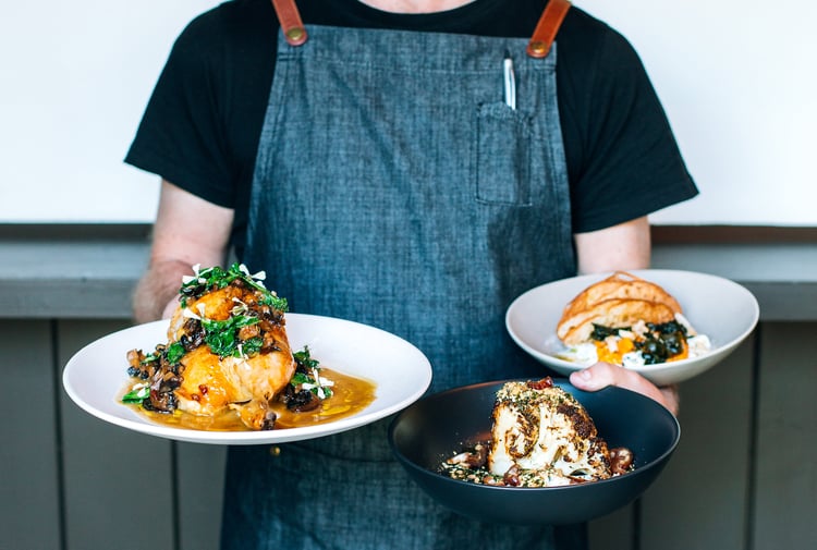 A staff member holding three plates of food at Kika in Wānaka.