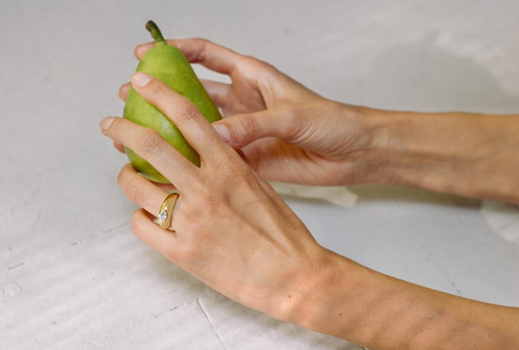 Two hands wearing rings holding a green pear.