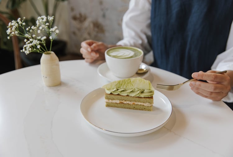Person sitting at table at Sweet Soul Patisserie with a cup of matcha latte and a beautiful matcha flavoured patisserie