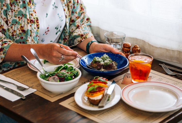 A woman sitting at a table with plates of food at Ombra Wellington.