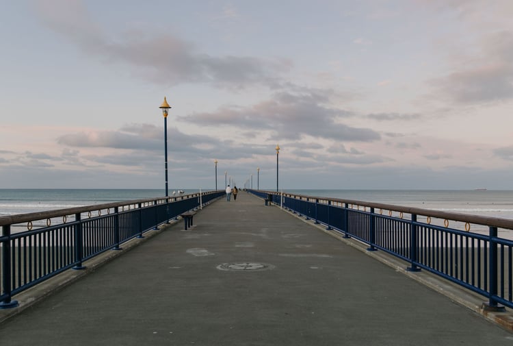 A couple walking along New Brighton pier in the evening with pinky skies and calm waters in the background