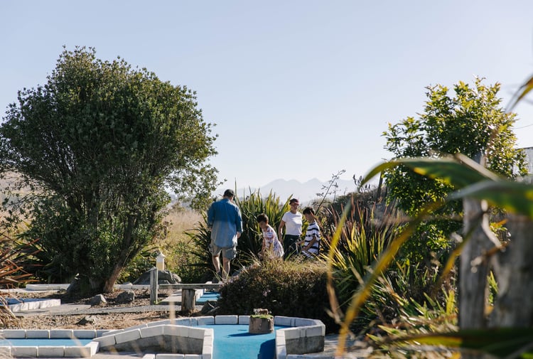 Kids playing mini golf with their parents on a sunny day.