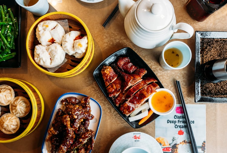 Table full of plates of Asian dishes and chopsticks.