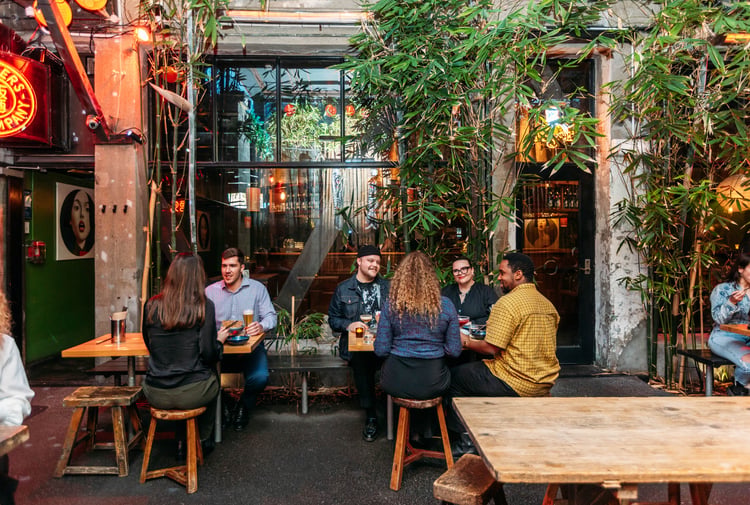 People dining outside by a building covered in vines.
