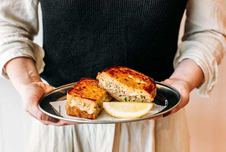 A person holding a plate of grilled cheese and tuna toasted sandwich.