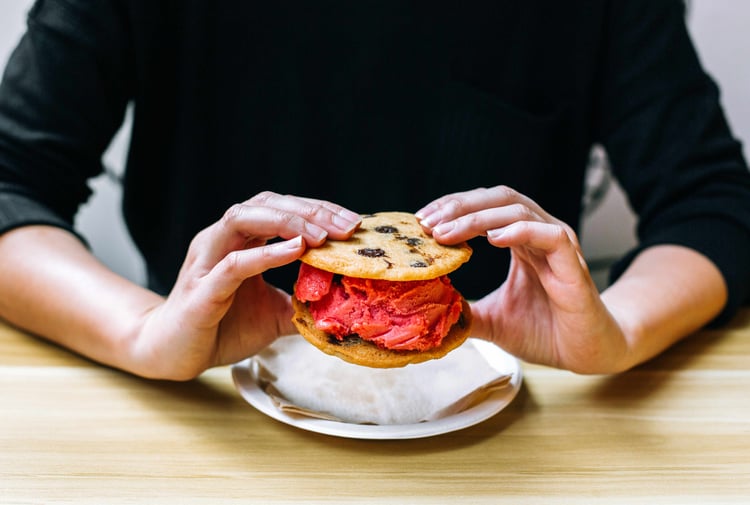 Two hands holding an ice cream cookie sandwich.