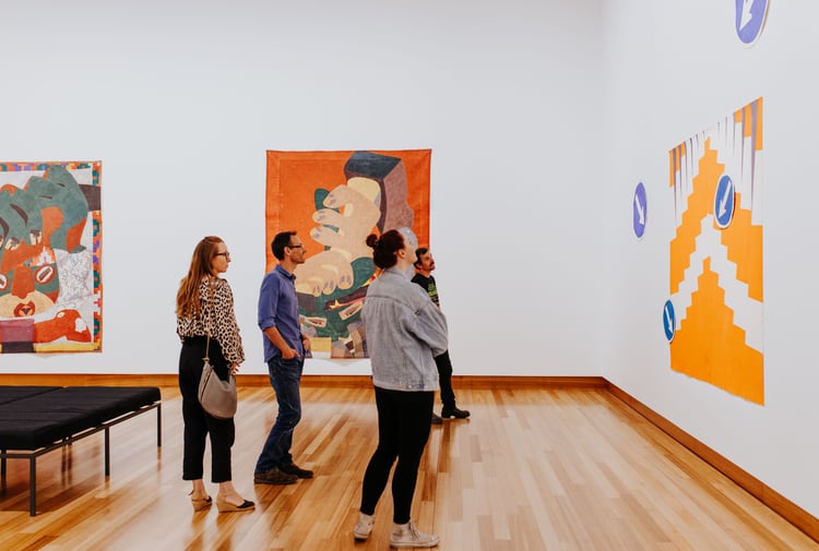 A group of adults looking intently at a colourful painting on a wall at Christchurch Art Gallery.