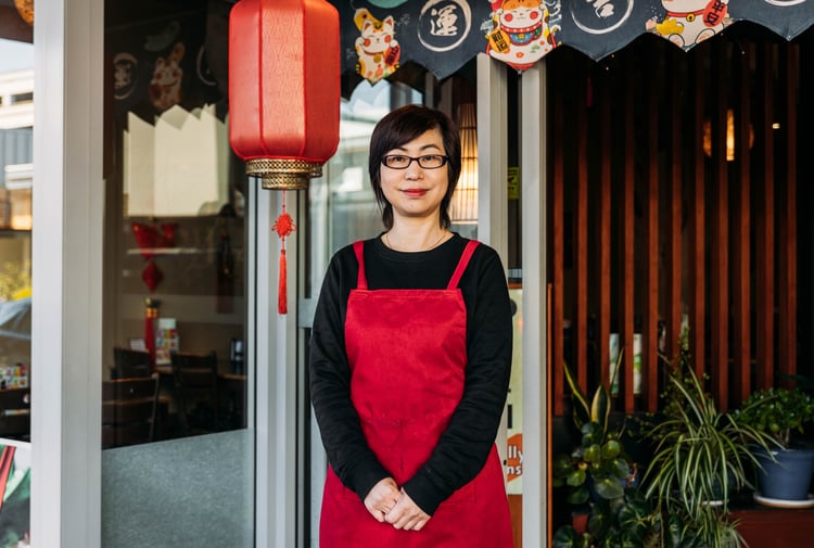 A woman dressed in red and black standing outside a Chinese restaurant smiling to camera.