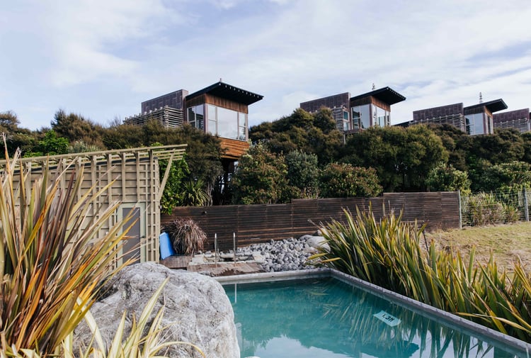 Wooden apartments set behind a swimming pool on a sunny day.