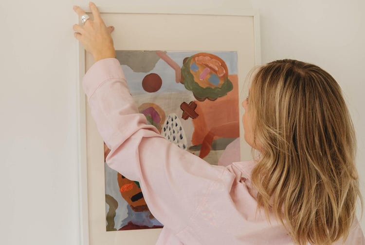 Woman hanging art print on the wall by Mathilde Langevin.