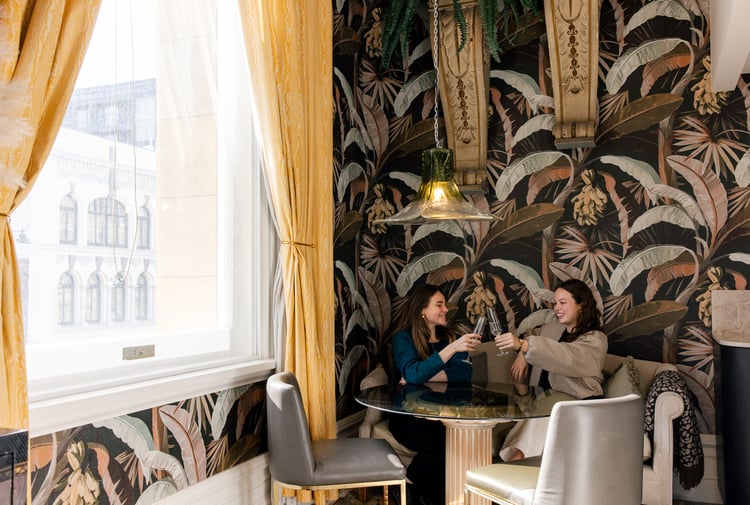Two women toasting their wine glasses sitting at a table.