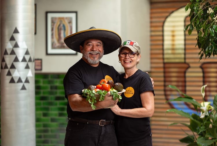 A man and woman holding a bowl of fresh vegetables smiling to camera.
