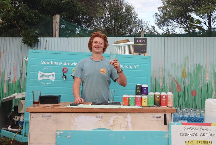 A man holding a beer and smiling to camera outside.