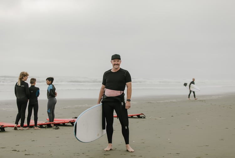 Hamish Evans at the beach smiling to camera whilst wearing a wet suit.
