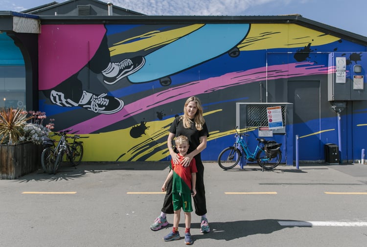 A woman and her son standing in front of a colourful mural painted on the exterior of a building.