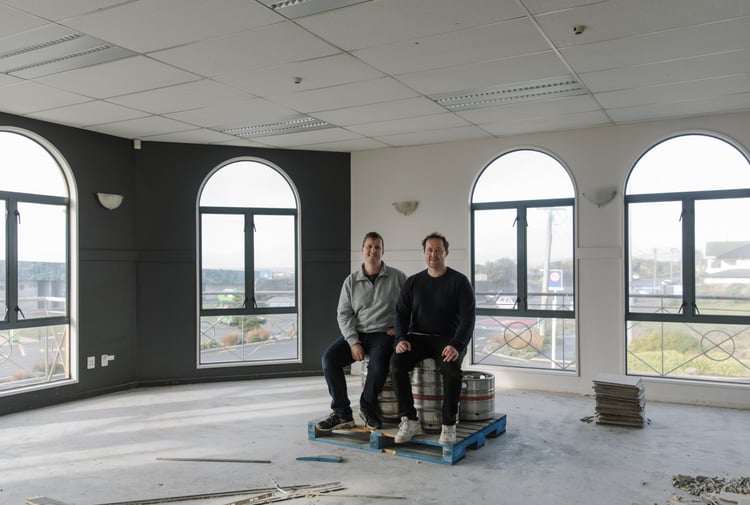 Two men sitting in an empty room smiling to camera.