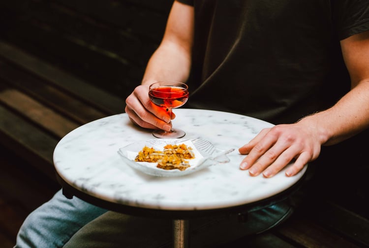 A hand holding a glass of rose next to a plate of food.