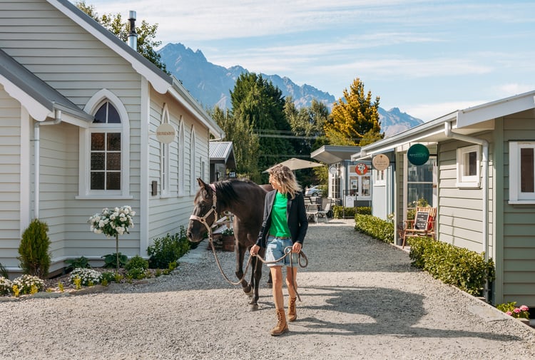 A woman and horse walking down a little country lane on a sunny day.