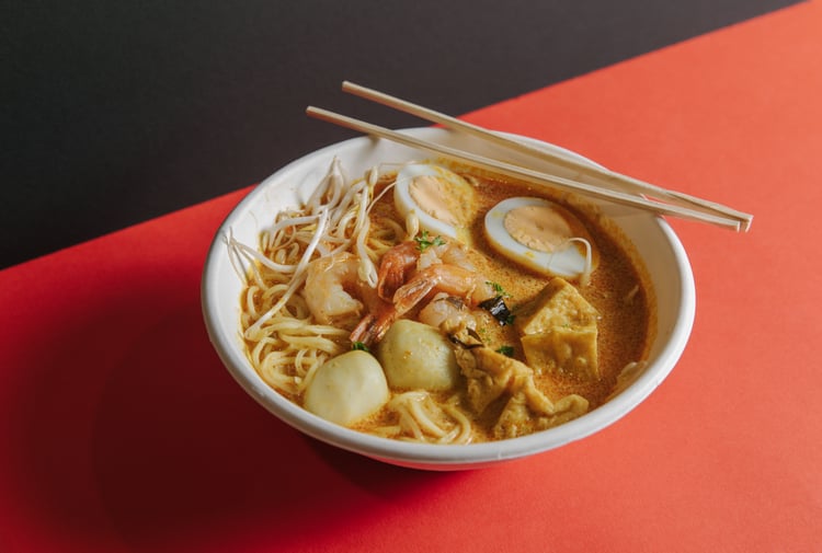 A plate of laksa on an orange table.