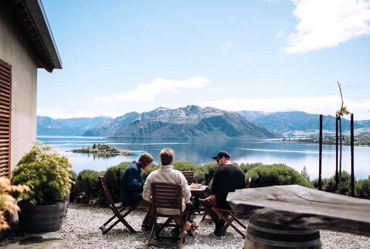 Three men are sitting at an outdoor table overlooking the lake.