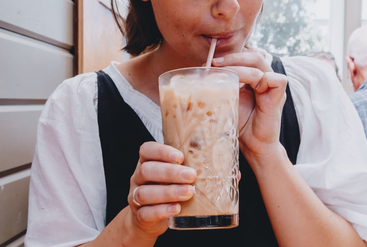 Close up of a woman sipping on an iced coffee in a big glass.