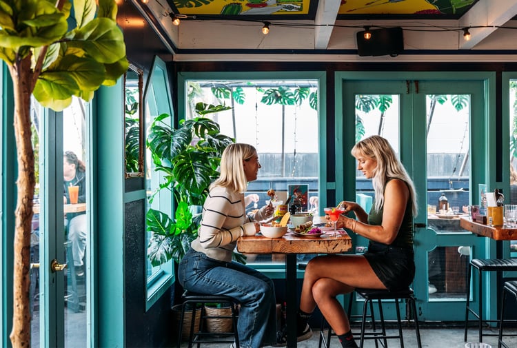 Two women dining at a high table inside a green painted room.