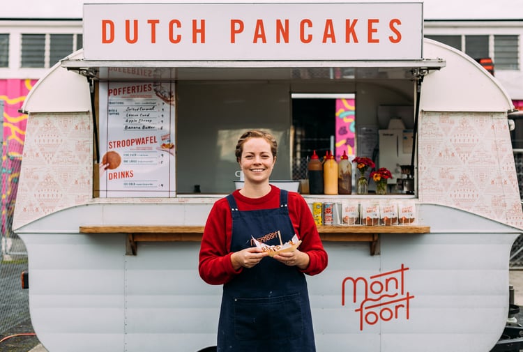 A woman holding Dutch pancakes in front of a white caravan.