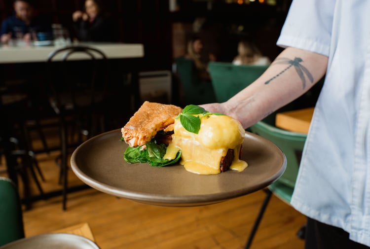 Someone holding a plate of eggs hollandaise with smoked salmon on the side