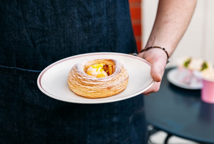 A hand holding a pastry on a plate.