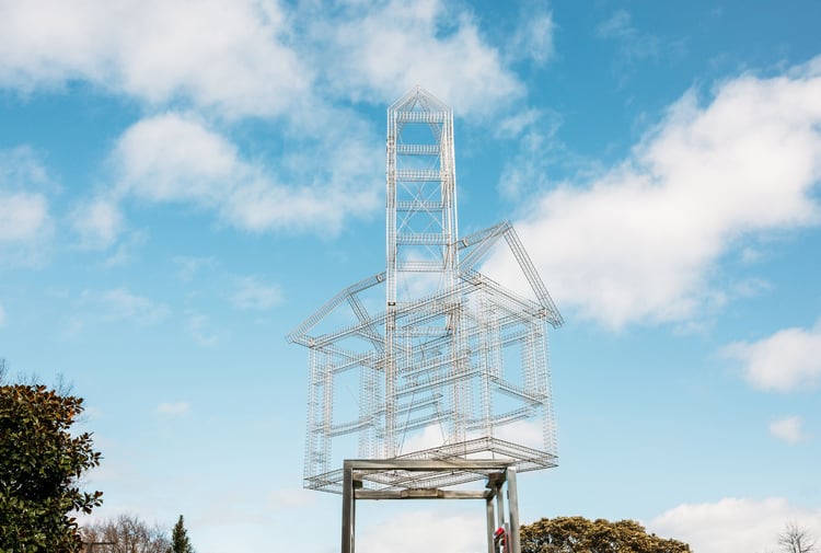 A sliver metal sculpture of a house frame on stilts.