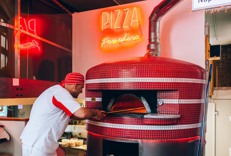 A man putting a pizza in a wood fired oven.