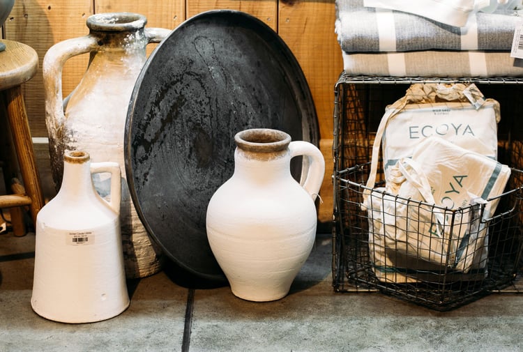 Two tall white concrete look vases on the floor next to a wire basket.