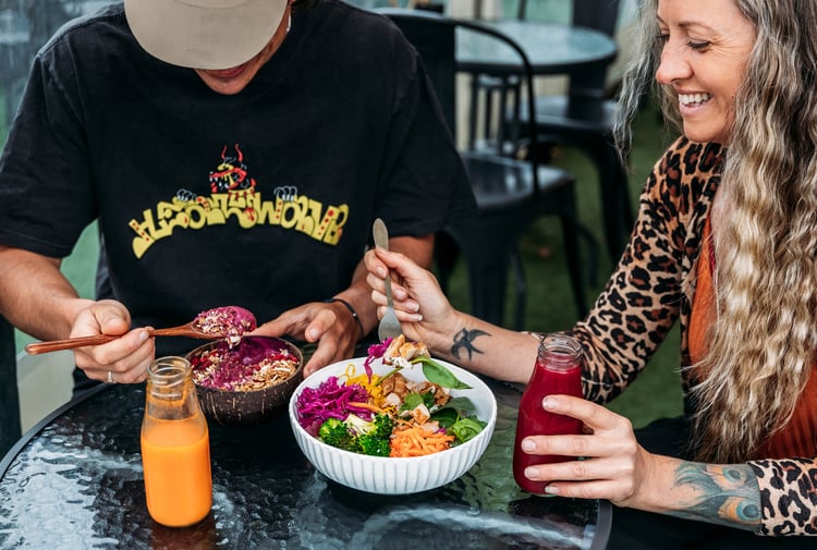 Two customers are eating buddha bowls and a glass bottle of juice is on the table.