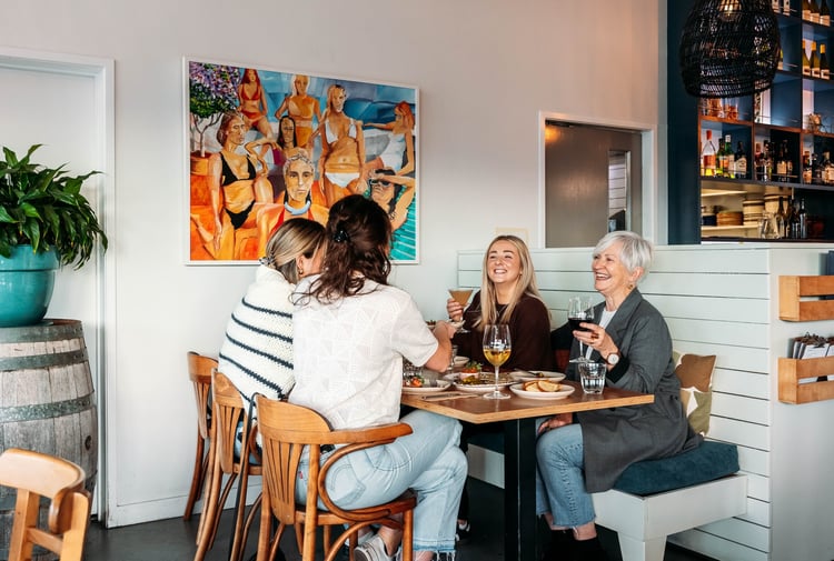 A group of women cheers their drinks over a table of food.
