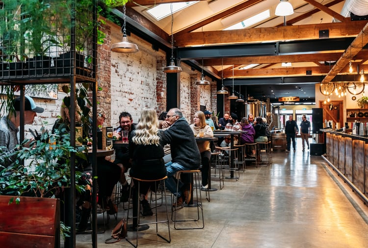 People sitting at high tops in a brick brewery building.