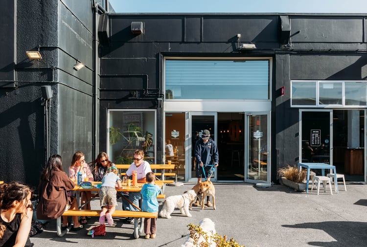 People and dogs hanging out outside a pub on a sunny day.