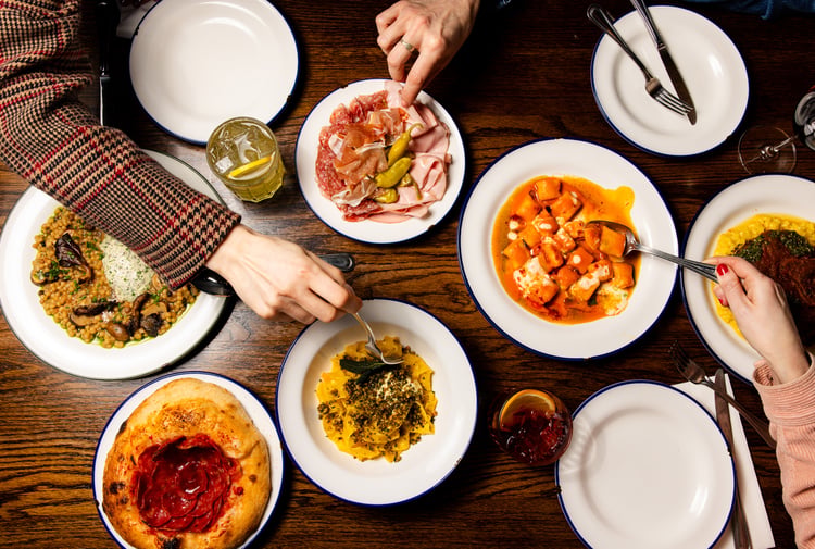 Flat lay of table full of Italian dishes at Bar Franco with people digging in with their forks