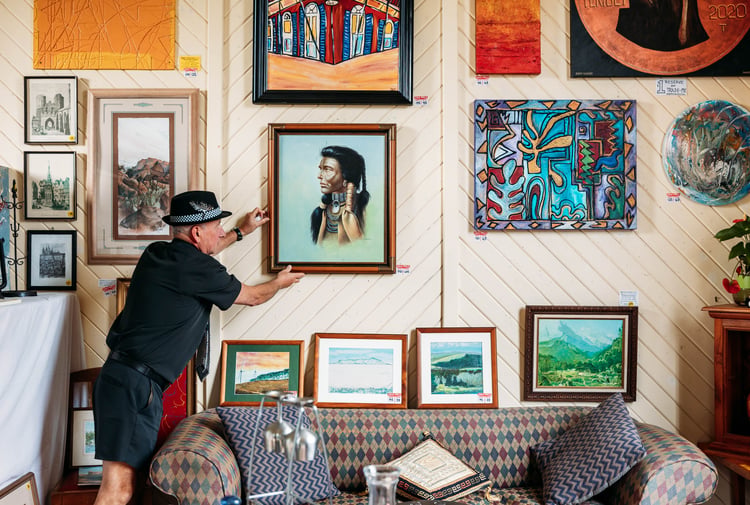 A man hanging art work on a wall inside a gallery.