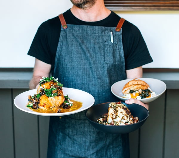 A staff member holding three plates of food at Kika in Wānaka.