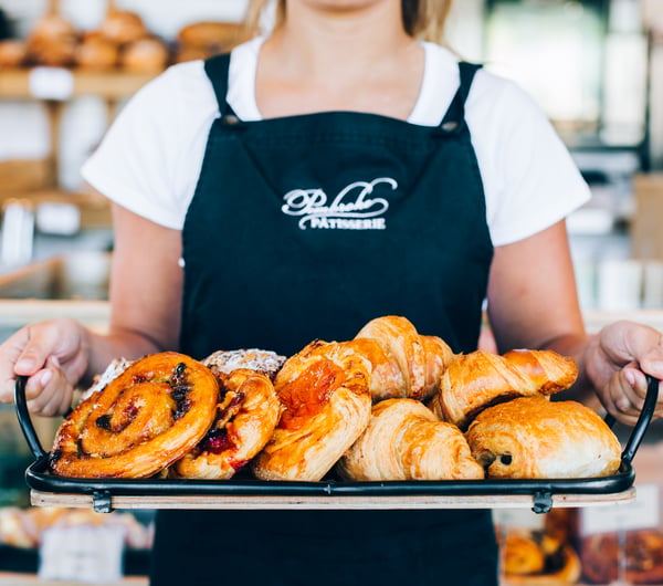 A staff member holding tray of freshly baked pastries.
