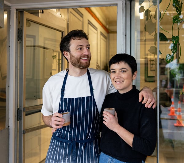 A man and woman looking at the camera outside their afe.