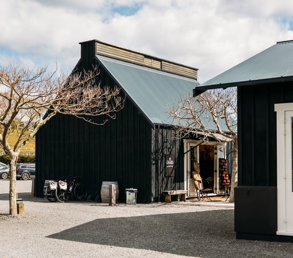 Two black barns outside in a sunny day.