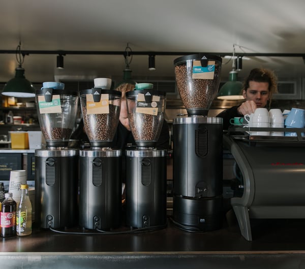 Two baristas working behind the coffee machine and four coffee bean grinders housing four different types of beans.