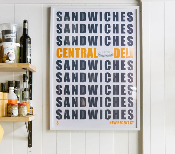 A large Central Deli Sandwiches poster framed on a wall.