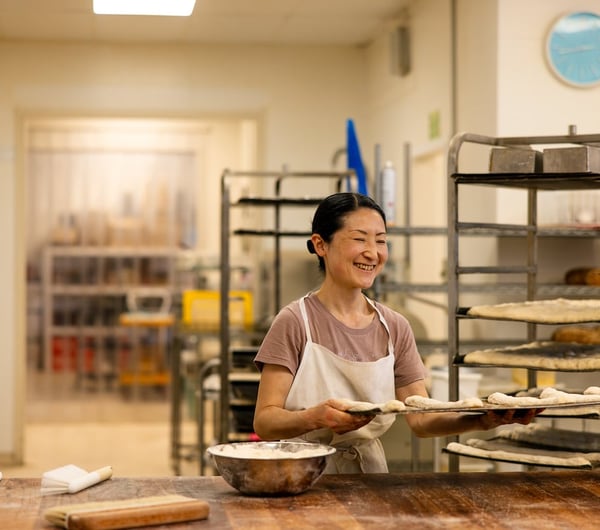 A female chef moves a tray of proving dough rolls.